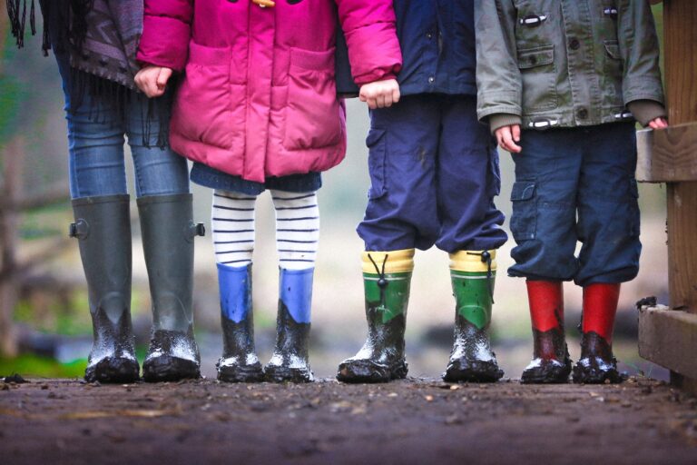 Nogi dzieci, ubrane w kalosze. Kolorowe ubrania kontrastują z deszczową aurą