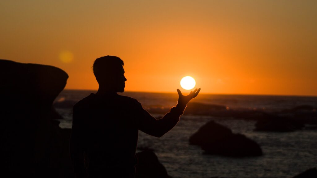 Mężczyzna na tle zachodzącego słońca, które "ujmuje" w dłoni