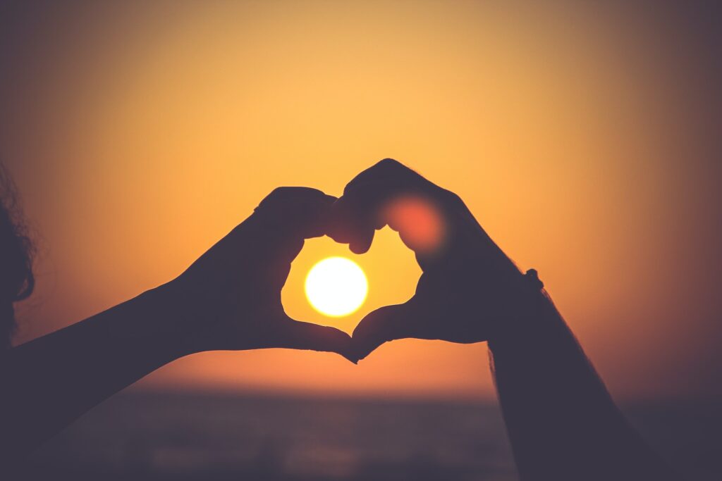 Dłonie ułożone w kształt serca obejmują zachodzące słońce