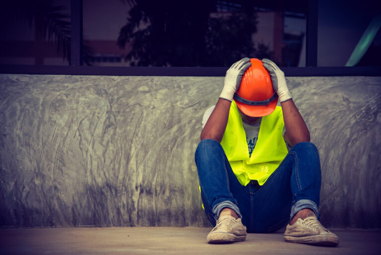 Smutny pracownik budowlany, siedzi ze spuszczoną głową, trzymając obie ręce na kasku