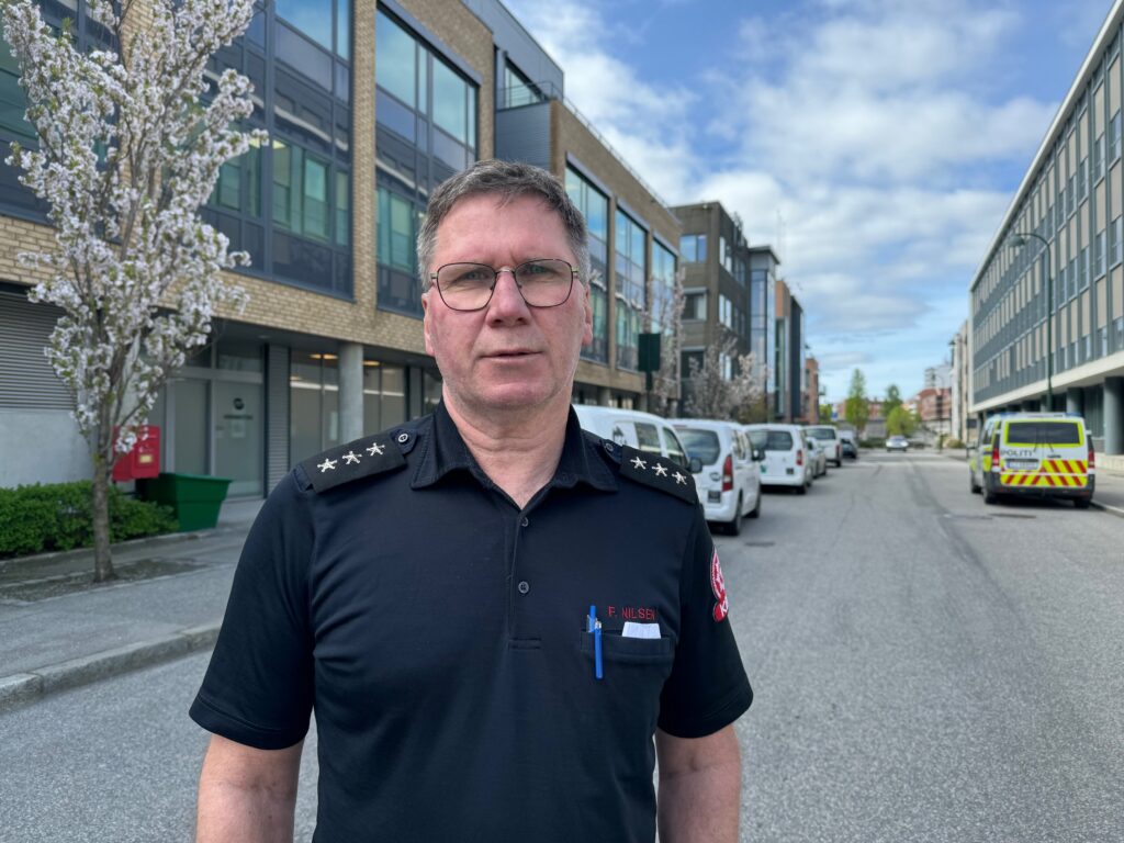 Frank Nilsen, szef straży pożarnej w regionie Kristiansand. Mężczyzna w okularach stoi na ulicy w Kristiansand w koszulce uniformu strażackiego.